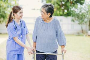 jovem enfermeira ajudando ásia Senior mulher andando. cuidador ajudando velho senhora paciente às enfermagem lar. mais velho andar com andador às casa Cuidado. foto