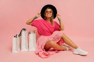 bonita sorridente mulher dentro Primavera na moda equipamento posando com branco compras bolsas dentro estúdio sobre Rosa fundo. foto