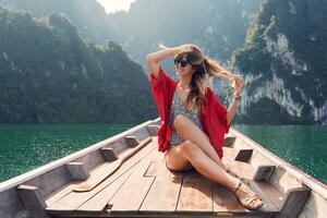 uma sexy jovem mulher vestindo uma bikini é sentado em uma pequeno barco perto uma tropical ilha. verão período de férias. foto