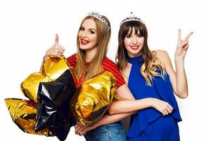 dois feliz adorável jovem mulheres com ouro Estrela em forma balões dentro mascarada coroa tendo Diversão , posando em branco fundo. a comemorar aniversário, Novo ano . foto