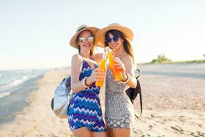 lindo meninas desfrutando seus coquetéis dentro garrafas em ensolarado verão surpreendente Califórnia de praia. foco em bebidas. foto