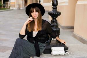 confiante à moda morena mulher posando dentro europeu cidade, caminhando em a rua. vestindo casual roupa, Preto chapéu e blusa. outono moda olhar. foto