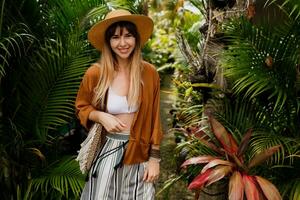 bem vestido mulher dentro perfeito humor de brincadeira posando dentro tropical jardim. bali feriados. boho acessórios. foto