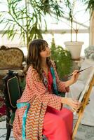 fêmea artista pintura em tela de pintura dentro dela arte estúdio. vestindo elegante boho roupa. foto