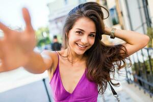 estilo de vida retrato do feliz morena mulher dentro à moda vestir fazer auto retrato dentro cidade Centro. alegre jovem menina tendo Diversão , desfrutando verão período de férias e finais de semana. foto