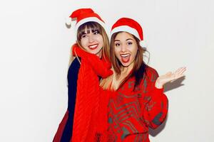 louco Novo ano festa humor. dois bêbado rindo mulheres tendo Diversão e posando em branco fundo dentro fofa mascarada chapéus. vermelho suéter e lenço. foto
