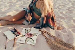 verão estilo de vida imagem do loiro mulher desenhando aguarela flor de escovar. artista sentado em a de praia. boêmio roupa. foto