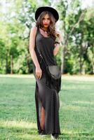 verão moda retrato do r elegante mulher com perfeito ondulado cabelo dentro à moda elegante Preto chapéu e brilhante faço acima posando dentro a parque. rua estilo. foto