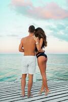 dois sensual amantes posando em a de praia sentado em de madeira branco cais . verão caloroso humor. tarde claro. foto