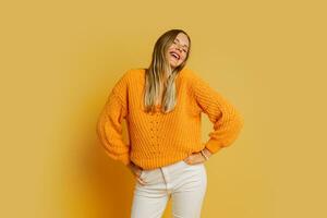 feliz loiro mulher dentro laranja à moda outono suéter posando sobre amarelo fundo dentro estúdio. foto