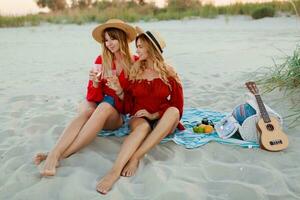 dois bonita mulheres dentro vermelho verão equipamento abd Palha chapéus desfrutando piquenique em a de praia. verão humor. foto