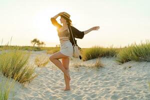 feliz europeu mulher dentro à moda boho verão vestem caminhando em a de praia. caloroso pôr do sol cores.palha chapéu. foto