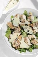 Salada Caesar de frango orgânico com queijo parmesão e croutons no fundo da mesa branca foto