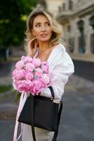 fechar acima retrato do elegante atraente loiro mulher segurando surpreendente Rosa ramalhete com piões. caminhando ao ar livre dentro europeu cidade. foto