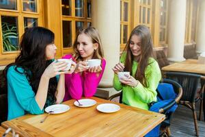 fechar acima estilo de vida retrato do três lindo jovem mulheres sentado dentro cafeteria e desfrutando quente tee . vestindo brilhante néon amarelo , Rosa e azul à moda suéter .feriados, Comida e turismo conceito . foto