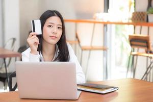 jovem mulher asiática segurando um cartão de crédito e compras online. foto