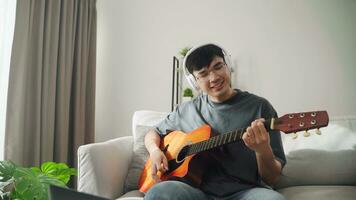 jovem bonito homem jogando acústico guitarra sentado em a sofá dentro a vivo quarto às lar. foto