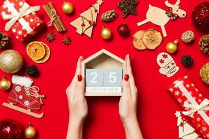 vista superior das mãos femininas segurando o calendário em fundo vermelho. dia vinte e cinco de dezembro. decorações de férias. conceito de tempo de natal foto