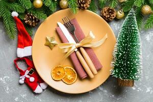 vista superior do garfo, faca e prato cercado com abeto e decoratoins de natal em fundo de cimento. véspera de ano novo e conceito de jantar de férias foto