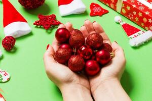 vista superior de um monte de bolas de ano novo em mãos femininas no fundo verde feito de decorações festivas. conceito de tempo de natal foto