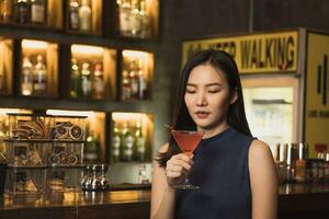 mulher asiática bebendo um coquetel em um bar à noite. foto