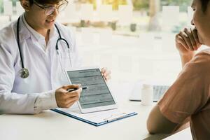 médico asiático falando com o paciente na clínica enquanto usa o tablet explicando a condição do paciente e o resultado do tratamento. foto