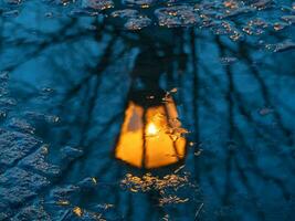 borrado Antiguidade lanterna brilha amarelo e é refletido dentro uma Primavera poça. urbano cartão postal abstrato visualizar. foto