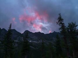 Sombrio silhuetas do montanhas contra uma brilhante Rosa pôr do sol céu. vermelho pôr do sol sobre majestoso montanhas. pôr do sol dentro magenta tons. atmosférico roxa panorama com uma grande altitude Nevado montanha vale. foto