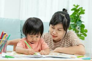 feliz Ásia mãe jogando Aprendendo pintura para pequeno garota. engraçado família é feliz e animado dentro a casa. mãe e filha tendo Diversão gastos Tempo junto. feriado, atividade foto