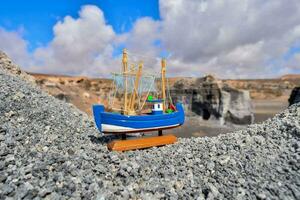 uma pequeno brinquedo barco senta em topo do uma rochoso penhasco foto