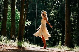 uma jovem com um vestido branco e um chapéu de palha caminha pela floresta foto