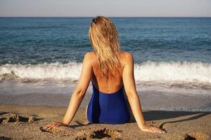 jovem tomando banho de sol na praia tropical. mulher em um maiô azul foto