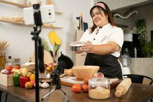 jovem atraente ásia mulher é blogging para dela cozinha canal sobre caseiro pizza enquanto transmissão conectados para webinar classe mestre lição. vlogger transmissão viver vídeo conectados ensino cozinhando foto