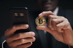 empresário segura bitcoin dourado usando smartphone com gráfico comercial. foto