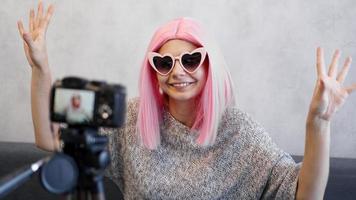 garota feliz blogueira com perucas rosa na frente da câmera em um tripé foto