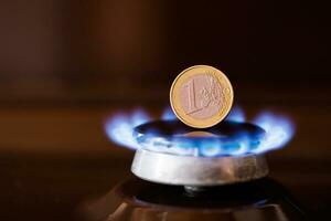 queimador de fogão a gás com uma moeda de euro em pé verticalmente em cima, queimando gás natural com chama azul foto