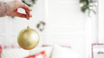 mão segurando enfeites de bola de ouro no fundo da árvore de Natal foto