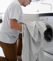 jovem colocando roupas na máquina de lavar
