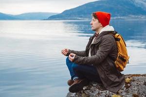 homem viajante em posição meditativa sentado em uma costa rochosa foto