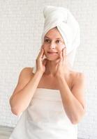 Mulher jovem sorridente e feliz usando toalhas de banho brancas fazendo procedimentos de spa foto