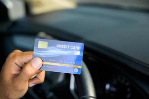 mão homem segurando um cartão de crédito dentro do carro.