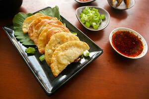 frito wonton. Wonton em prato com Pimenta óleo. camarão ou carne bolinho de massa sopa com mostarda , verde cebolas, em mesa foto