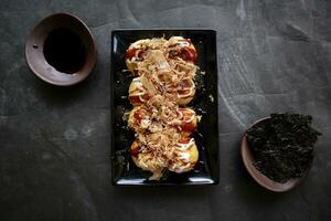 takoyaki é uma japonês comida, fez a partir de trigo farinha massa, polvo carne, ou de outros recheios, servido com molho, maionese e cobertura dentro a Formato do katsuobushi ou madeira peixe aparas de madeira. foto