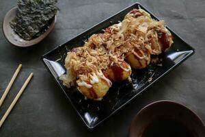 takoyaki é uma japonês comida, fez a partir de trigo farinha massa, polvo carne, ou de outros recheios, servido com molho, maionese e cobertura dentro a Formato do katsuobushi ou madeira peixe aparas de madeira. foto