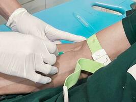 uma masculino enfermeira é injetando uma dor apaziguador anestésico para dentro uma pacientes mão foto