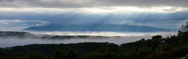 panorâmico tiro do Sol raio dentro a manhã com névoa fluxo através a montanha vale, chiangmai, durante chuvoso temporada, Tailândia foto