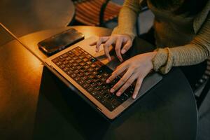 mulher usando computador portátil, procurando a rede, navegando Informação, tendo uma local de trabalho às casa com caloroso iluminação em volta. foto