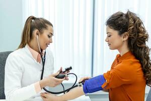 medindo sangue pressão. jovem mulher ter uma Visita com fêmea médico dentro moderno clínica. medindo sangue pressão. pressão medidor. hipertensão e Alto coração taxa foto