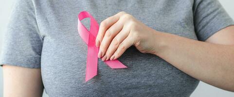 mulher de camiseta cinza prende a fita rosa no peito. Mês de conscientização do câncer de mama. promoção de campanha contra o câncer. foto