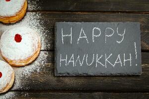 Feliz Hanukkah. sobremesa tradicional sufganiyot em fundo escuro de madeira. rosquinhas, velas e presentes. comemorando feriado judaico. foto